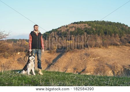 A man with a beard walking his dog in the nature, standing with a backlight at the rising sun, casting a warm glow and long shadows against the background of the gorge and trees on caucazus