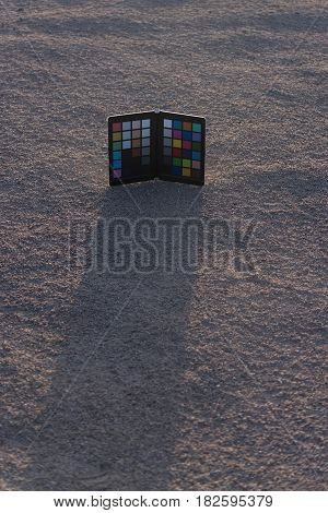 Colorchecker or color rendition chart palette board for photo camera on sandy ground or soil desert surface on grey sand background. Professional photography equipment copy space