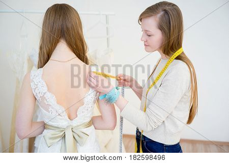 Young bride with wedding assistant making final touch on wedding dress