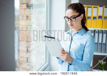Concentrated Woman Standing Near The Window At Her Office Hilding Digital Tablet And Reading Informa