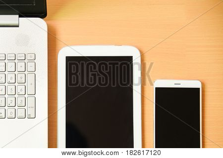 Soft focus notebook computer with taptet and smarth phone on wooden desk background