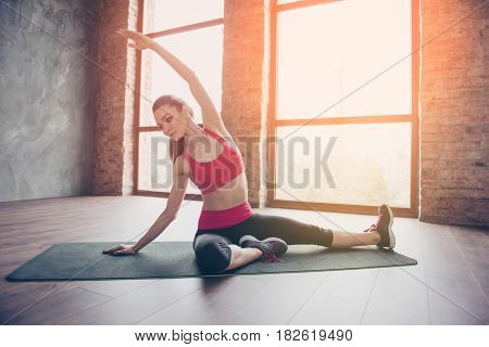 Young Sportwoman Is Making Stretching On Green Mat On The Floor Of Sunny Room. She Is Focused And Se