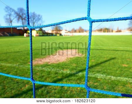Detail of yellow blue crossed soccer nets soccer football in goal net with grass on outdoor playground in the background.