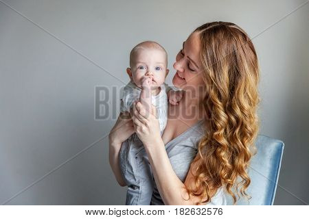Young mother holding her newborn child. Woman and new born boy relax in a white bedroom with blue chair. Mother breast feeding baby. Family at home
