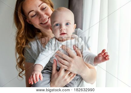 Young mother holding her newborn child. Woman and new born boy relax in a white bedroom near the windiow. Mother breast feeding baby. Family at home. Young mother playing whith her newborn son