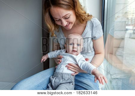 Young mother holding her newborn child. Woman and new born boy relax in a white bedroom near the windiow. Mother breast feeding baby. Family at home. Young mother playing whith her newborn son