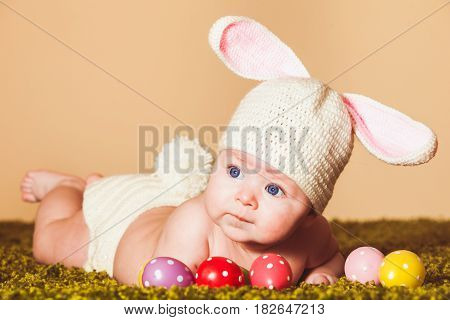 Three months baby lying on his stomach as a Easter bunny on the grass with eggs