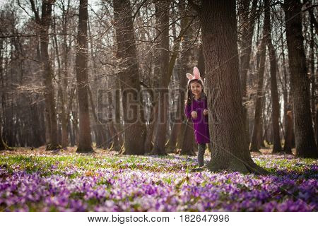 Little girl with banny ears peeping from behind a tree in the park