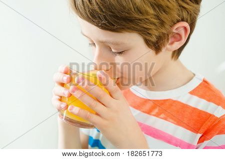 Young teenager boy drinking orange juice indoors at white background