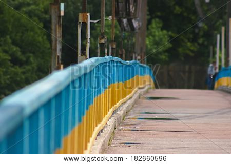 Blue and yellow painted bridge as ukrainian flag over river in autumn forest