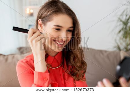 beauty, makeup, cosmetics and people concept - happy smiling young woman with brush applying bronzer or blush to her face and looking to mirror at home