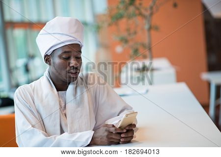 Sudanese business man in traditional outfit using mobile phone in office.