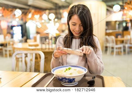 Woman taking photo in her ramen in restaurant