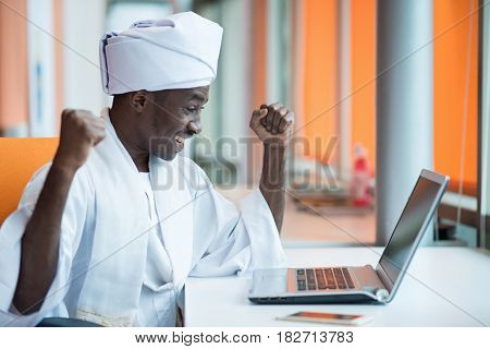 Sudanese business man in traditional outfit using mobile phone in office.