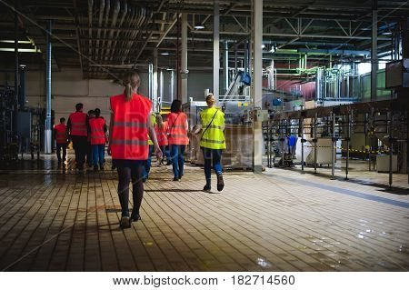 Blonde Woman In Overalls, On The Tour Of The Brewery Plant In Industrial Premises, Amid Crowds Of Pe