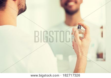 perfumery, beauty and people concept - close up of happy smiling young man with perfume looking to mirror using scent at bathroom