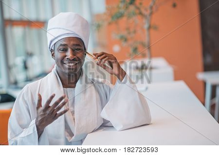 Sudanese business man in traditional outfit using mobile phone in office.