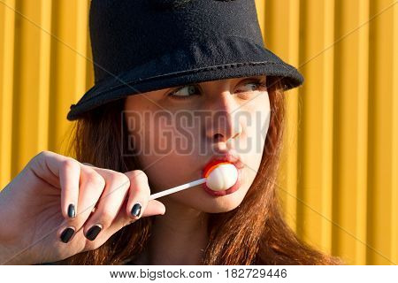 Cheerful Stylish Young Girl In Hat, And Jeans Jacket With Candy On Stick, Chupa Chups, On Sunny Day