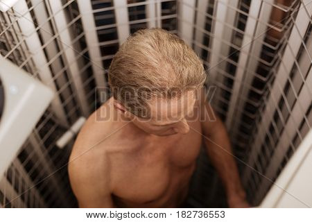 Enjoying indoor tanning. Involved handsome athletic man enjoying wellness procedure in the beauty salon and getting into tanning both while expressing confidence