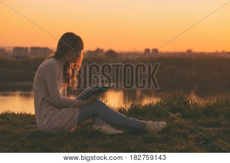 Woman enjoys reading a book with a sunset over the city.