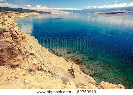 Mountain biker riding on bike in summer inspirational mountains and sea landscape. Man cycling MTB on enduro trail track at seaside and rocky dirt path. Sport fitness motivation and inspiration.