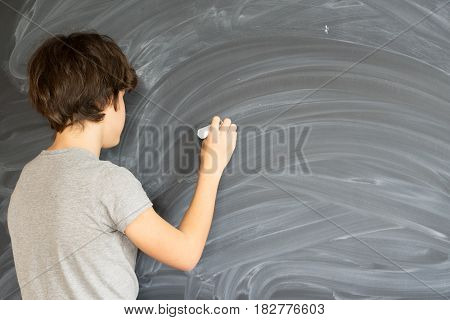Teen Boy with chalk in hand writting on empty black board