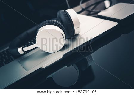 Modern Laptop Computer Setup with Wireless Headphones on Glassy Desk.