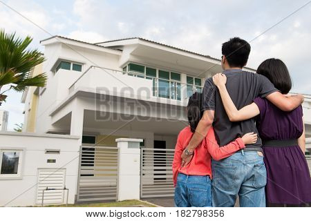 Parents and kid standing in front of dream house in modern residential houses