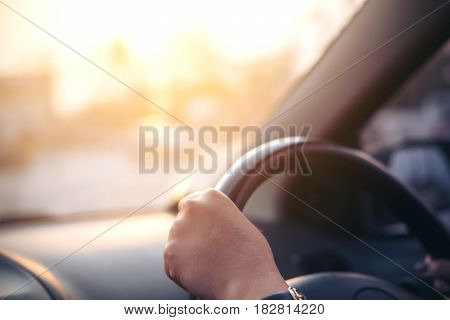 Woman's hands holding on black steering wheel while driving a car during sunset