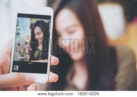 A man using white smart phone taking a picture of a beautiful woman in wooden vintage cafe