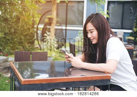 A beautiful asian woman enjoy using on smart phone with feeling relax and smiley face in outdoor and green nature background