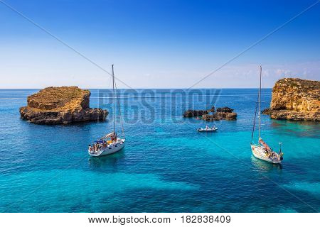 Comino Malta - Sailing boats at the beautiful Blue Lagoon at Comino Island with turquoise clear sea water blue sky and rocks in the water