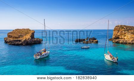 Comino Malta - Sailing boats at the beautiful Blue Lagoon at Comino Island with turquoise clear sea water blue sky and rocks in the water