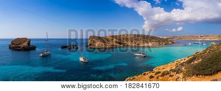 Comino Malta - Panoramic skyline view of the famous and beautiful Blue Lagoon on the island of Comino with sailboats traditional Luzzu boats and tourists enjoying the azure mediterranean sea water and sunshine