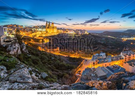 Il-Mellieha Malta - Beautiful panoramic skyline view of Mellieha town after sunset with Paris Church and Mellieha beach at background with blue sky and clouds