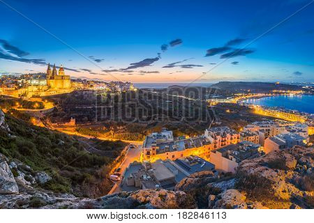 il-Mellieha Malta - Beautiful panoramic skyline view of Mellieha town after sunset with Paris Church and Mellieha beach at background with blue sky and clouds