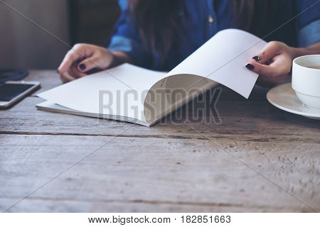 A woman opening and reading a book with coffee cup on wooden table in vintage cafe