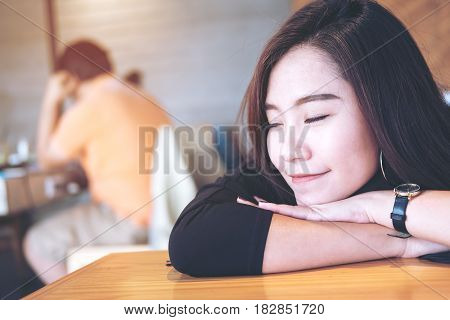 A beautiful asian woman sit with chin resting on her hands and closing her eyes in wooden cafe
