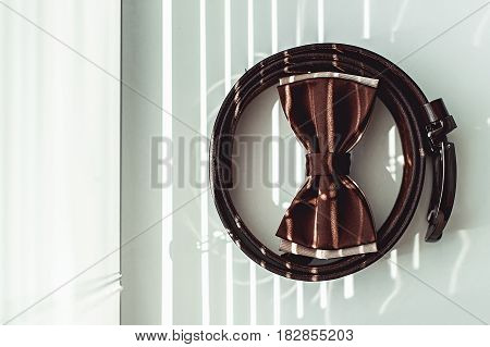 Brown bow tie and belt. Grooms wedding morning. Close up of modern man accessories on the window sills with shutters. Look from above