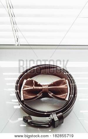 Brown bow tie and belt. Grooms wedding morning. Close up of modern man accessories on the window sills with shutters. Look from above