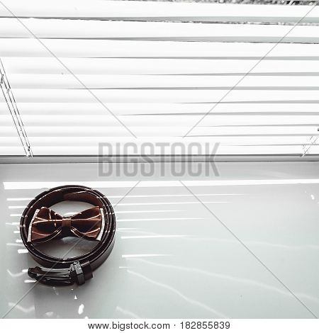 Brown bow tie and belt. Grooms wedding morning. Close up of modern man accessories on the window sills with shutters. Look from above