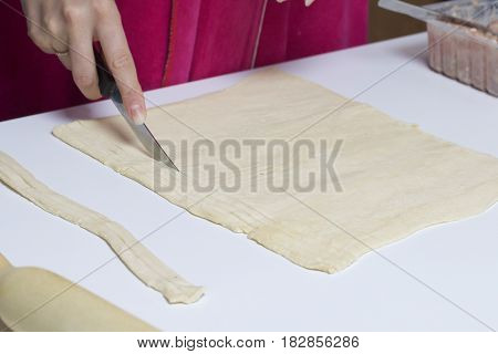 Stages Of Preparation Of Meat Glomeruli. A Woman Slices Thin Strips Of Dough. Next To The Table Is A