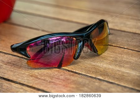 Red to yellow gradient sun glasses lying on wood table outside