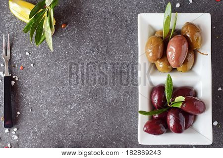 Plate of black and green olives on a grey abstract background with the copy space. Healthy food concept
