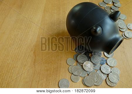 Lot of coins and black piggy bank on wood table