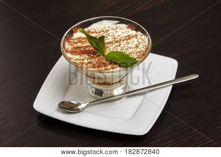 Tiramisu creme cake dessert in glass with mint leaves on black wooden background