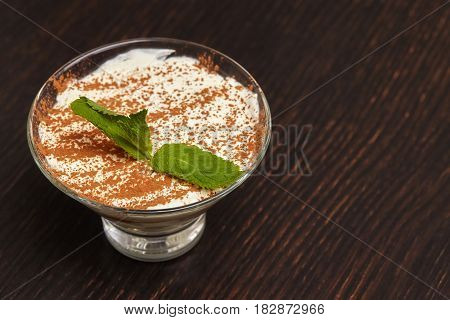 Tiramisu creme cake dessert in glass with mint leaves on black wooden background