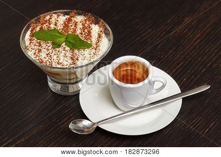 Tiramisu creme cake dessert in glass with mint leaves and coffee cup on black wooden background