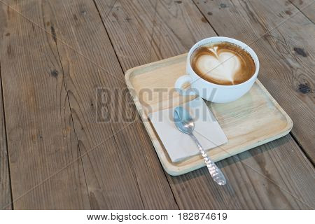 hot cappuccino coffee with napkin and spoon on wooden table in day light