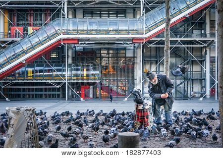 PARIS - January 4 2016: Unidentified elderly man feeding pigeons in front of Pompidou Centre in Paris France.